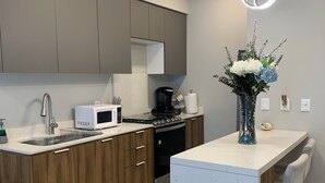 A modern kitchen with a built-in microwave, coffee maker, and stainless steel sink. - Alameda Apartment (Tijuana)