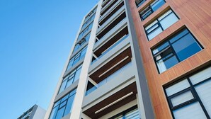 A modern high-rise building with multiple floors, large windows, and a mix of materials including wood and concrete. - Alameda Apartment (Tijuana)