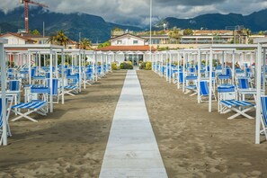 A beachside hotel with rows of blue and white sun loungers, a central walkway, and a mountain backdrop. - Casa Nadia 1.2 Km From Sea With Terrace & Parking (Massa)