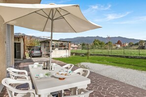 Un espace de restauration en plein air avec une table dressée pour deux personnes, un grand parasol et une vue sur le paysage environnant.