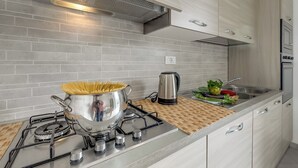 Une cuisine moderne équipée d’une cuisinière à gaz, d’une casserole de spaghettis, d’une bouilloire et de légumes frais sur le plan de travail.