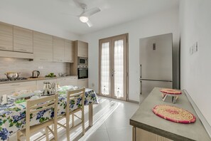 Une cuisine moderne avec des meubles en bois, une table à manger recouverte d’une nappe à motifs floraux et un réfrigérateur.