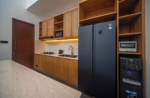 A kitchen with wooden cabinets, a black refrigerator, a microwave, a water dispenser, and a sink. - Brand New 2Bedroom Water Lily Villa Private Pool (Denpasar Selatan Bali)
