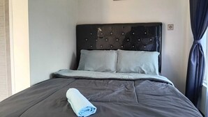 Cama bem arrumada com toalha enrolada, cabeceira escura e um quadro único na parede.