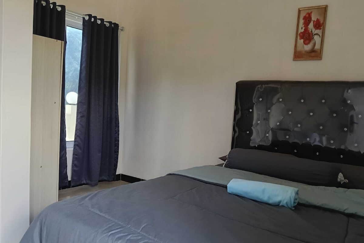 A bedroom with a bed, a window with curtains, and a painting on the wall.