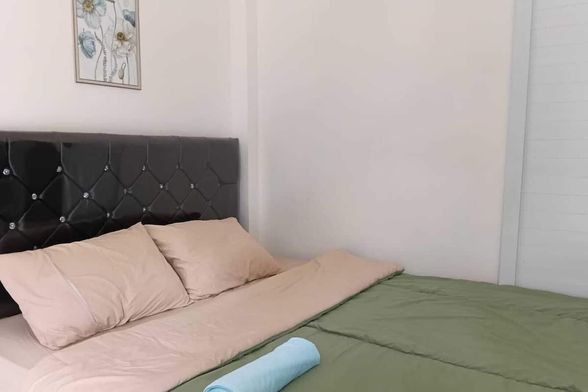 A bed with a tufted headboard, beige and green bedding, and a rolled-up towel.