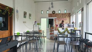Um café com mesas e cadeiras dispostas para acomodar pessoas, um balcão com um cardápio e uma parede com publicidade de café.