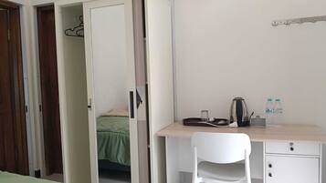 Quarto com cama, escrivaninha, cadeira, armário e pequena cozinha.