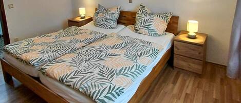 Ein Doppelbett mit blattgemusterten Bettwäsche, zwei Nachttische mit Lampen und ein Sonnenuntergangsgemälde an der Wand.