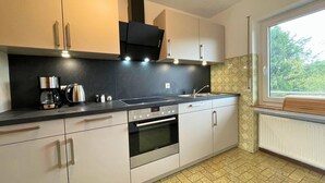 A modern kitchen with a built-in oven, a coffee maker, and a window with a view of greenery. - Holiday Home in Birresborn With Balcony (Birresborn)