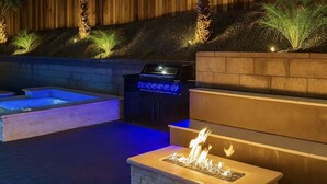 Un espacio al aire libre con un hoyo de fuego, una parrilla de barbacoa y luces colgantes.