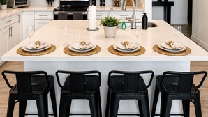 Una cocina moderna con armarios blancos, una isla central con taburetes, microondas, horno y pileta.