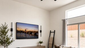 Una sala de estar moderna con un sofá seccional, una mesa de centro, un televisor montado en la pared, una planta en maceta y vistas a través de un ventanal grande.