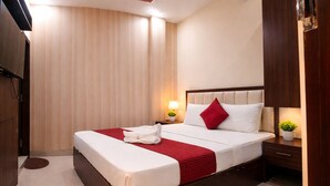 A hotel room with a large bed, wooden headboard, two bedside tables with lamps, a red throw blanket, and a small potted plant. - Hotel Grill Inn (Lucknow)