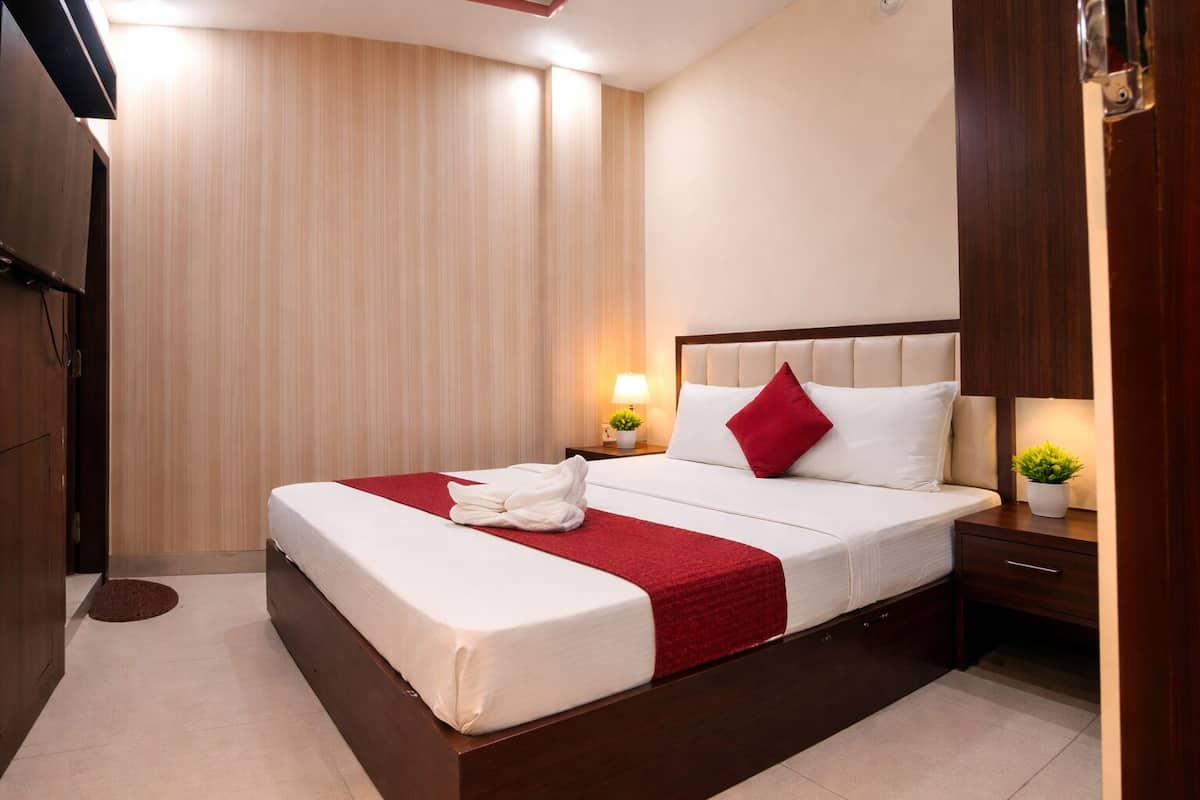 Habitación de hotel con una cama grande, cabecera de madera, dos mesitas de noche con lámparas, una manta roja y una pequeña planta en maceta.