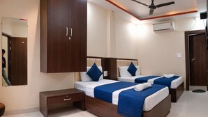 A hotel room with two beds, a wardrobe, a bedside table, an air conditioning unit, and a ceiling fan. - Hotel Grill Inn (Lucknow)
