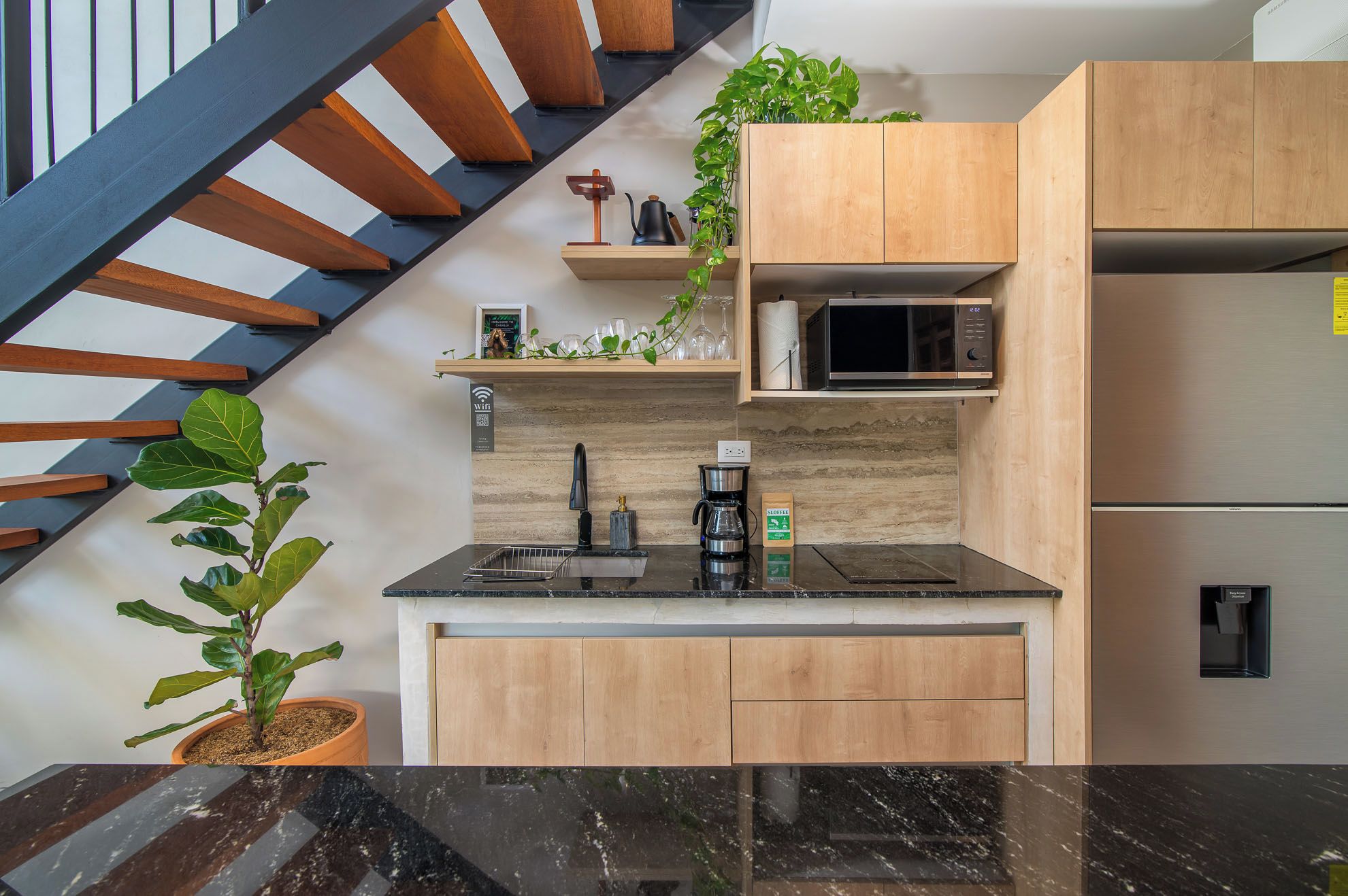 Une cuisine moderne avec un plan de travail noir, des meubles en bois, un four à micro-ondes et une machine à café.