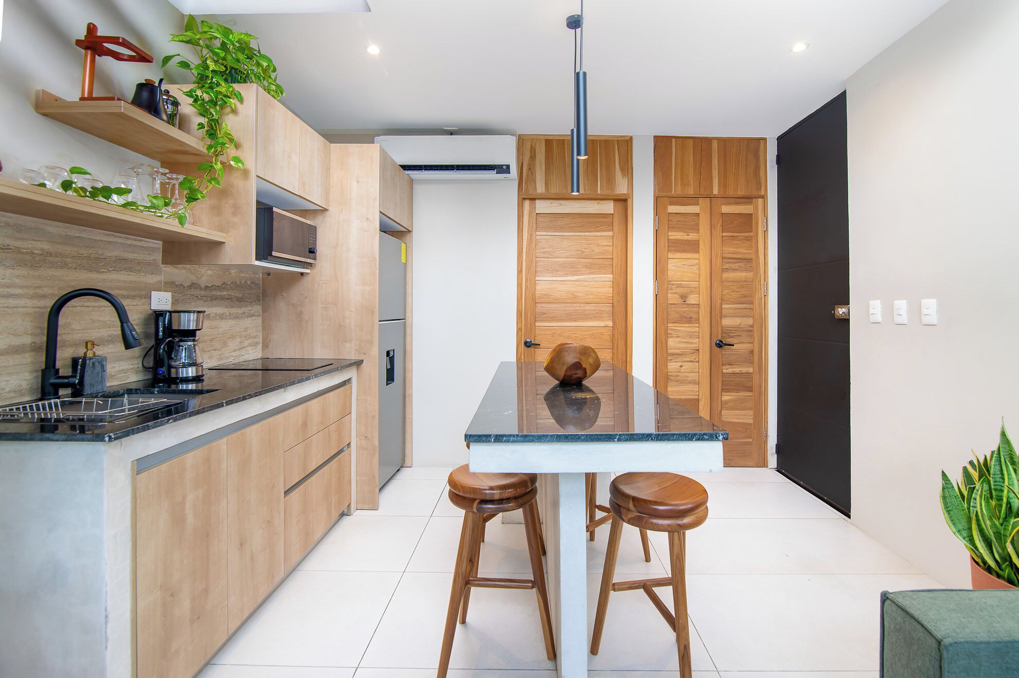 Una cocina moderna con armarios de madera, encimera negra, una cafetera y dos taburetes.