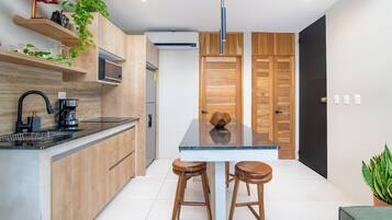 Una cocina moderna con armarios de madera, encimera negra, una cafetera y dos taburetes.