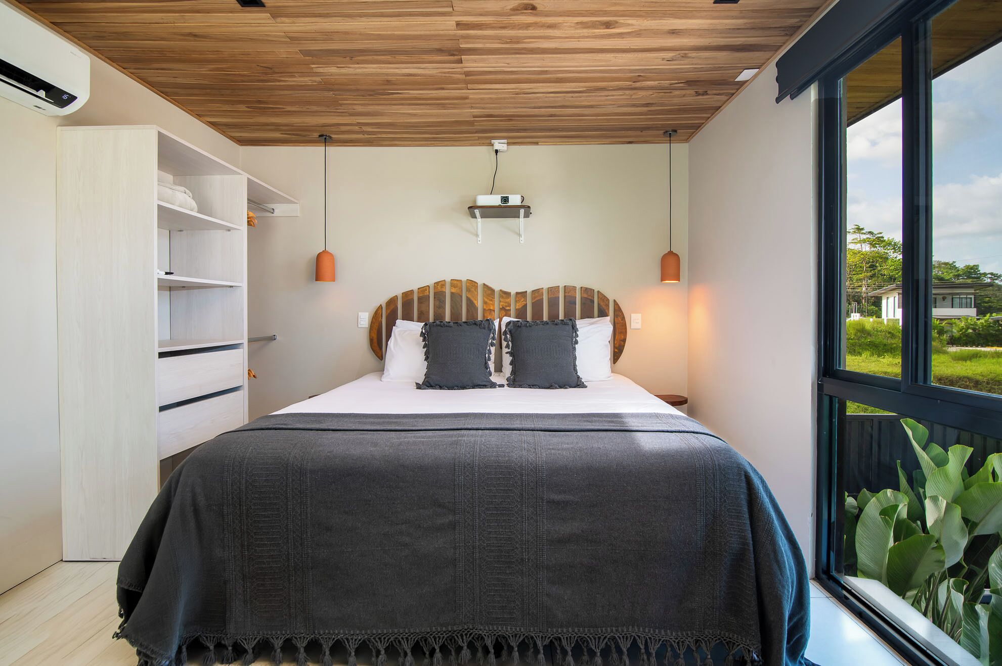 A bedroom with a bed, a wardrobe, a ceiling fan, and a view of greenery outside.