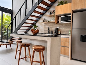 Una cucina moderna con isola centrale, sgabelli di legno, frigorifero in acciaio inossidabile e una scala con ringhiere nere.