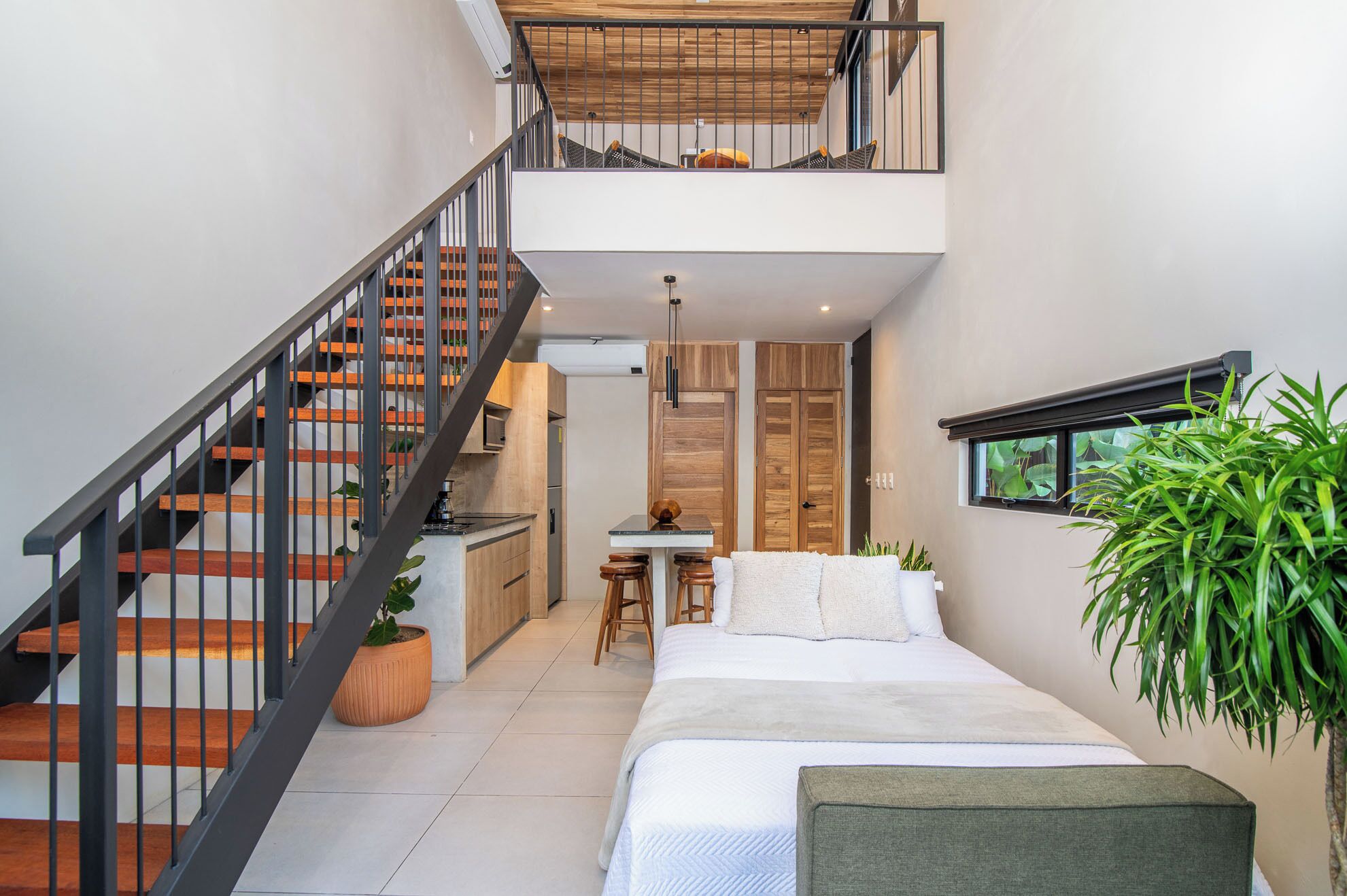 A compact, modern interior with a staircase, a kitchen area, a dining table, and a bed.