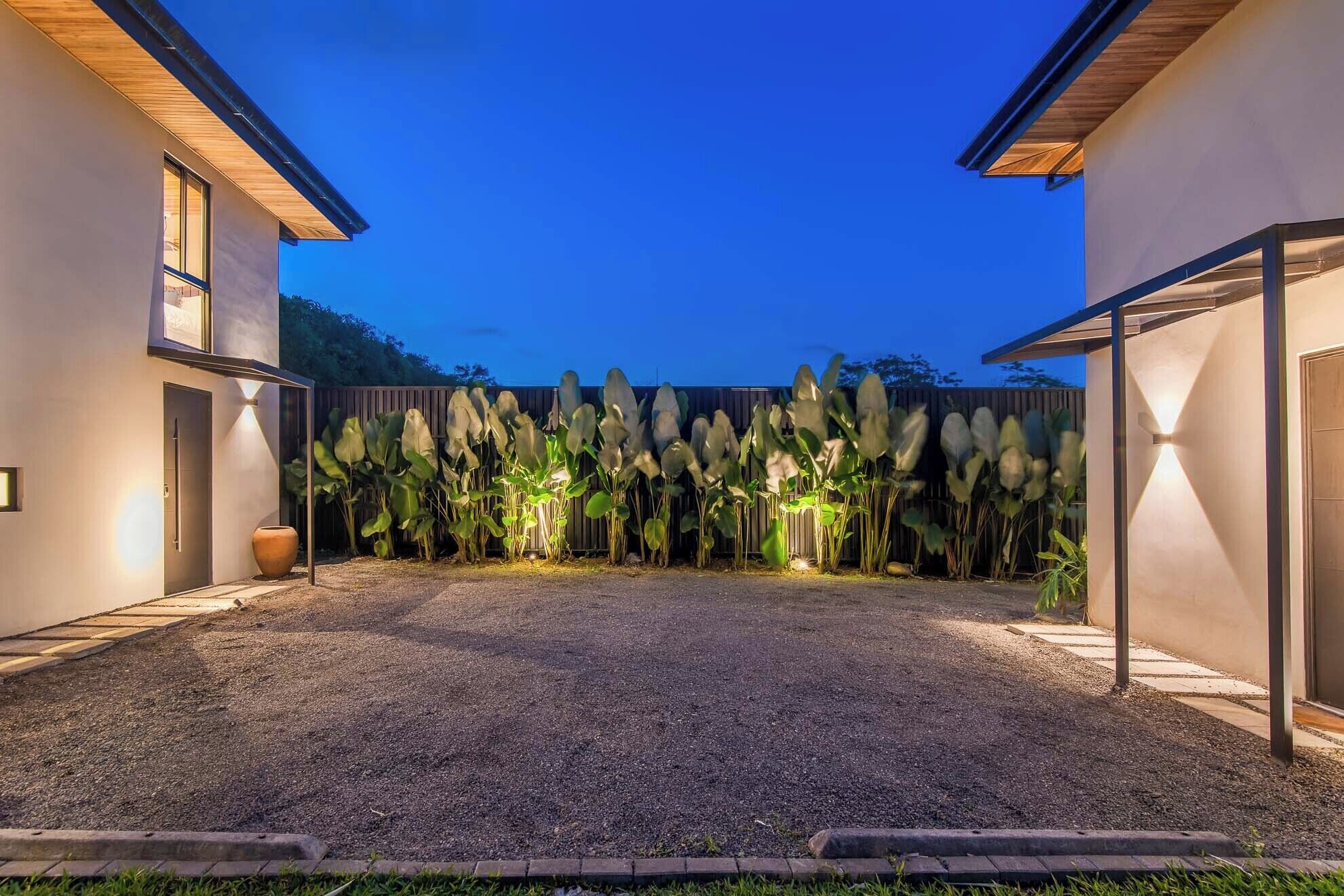 Una casa moderna con entrada de grava, cerca de madera y jardín iluminado.