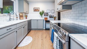 A modern kitchen with grey cabinets, a stainless steel stove, and a white tiled backsplash. - Grisham Getaway: Hot Tub + Game Room + Firepit + Kid & Pet Friendly (Bella Vista)