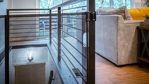 A room with a wooden floor, a grey sofa with a yellow cushion, and a metal gate. - Grisham Getaway: Hot Tub + Game Room + Firepit + Kid & Pet Friendly (Bella Vista)