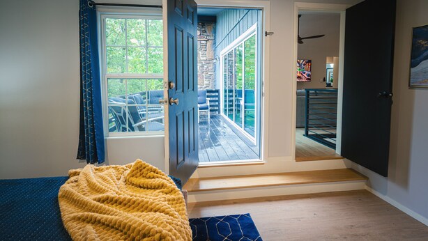 A room with a bed, a yellow blanket, a wooden floor, and a view of a deck through a door. - Grisham Getaway: Hot Tub + Game Room + Firepit + Kid & Pet Friendly (Bella Vista)
