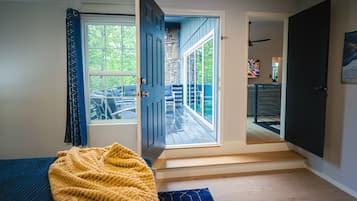 Een kamer met een bed, een gele deken, een houten vloer en uitzicht op een terras door een deur.