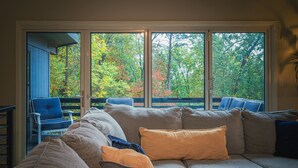 A living room with a large window, a sofa, and a chair. - Grisham Getaway: Hot Tub + Game Room + Firepit + Kid & Pet Friendly (Bella Vista)