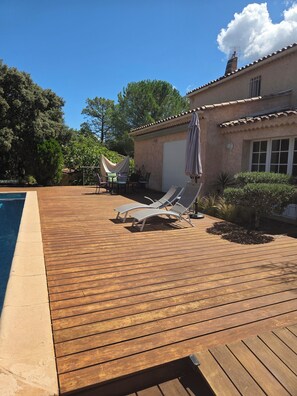 Eine Holzterrasse mit Liegestühlen und einem Poolbereich.