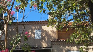 Un bâtiment rustique avec un toit en tuiles, un balcon doté d’une balustrade en métal et un arbre aux fleurs roses.