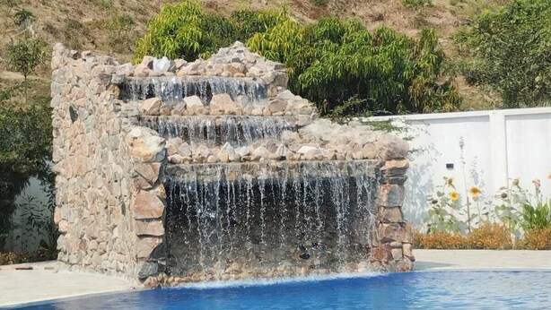 A swimming pool with a stone waterfall feature and a hillside in the background. - Venus Resort Bandarban (Bandarban)