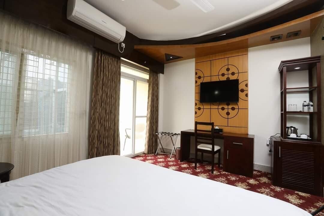 Habitación de hotel con una cama grande, un escritorio, un televisor montado en un panel de pared de madera y un armario.