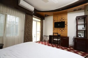 Habitación de hotel con una cama grande, un escritorio, un televisor montado en un panel de pared de madera y un armario.