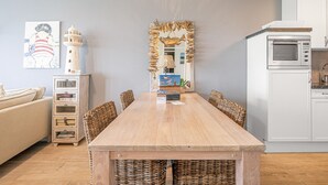 A dining area with a wooden table, wicker chairs, a white cabinet, and a kitchen with a microwave. - 4 Person Apartment With sea View (De Koog)
