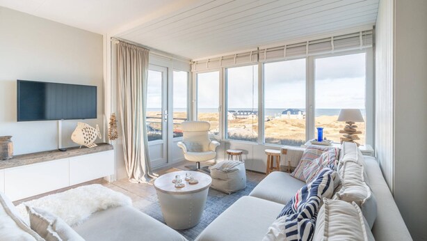 A modern living room with a large window, a flat-screen TV, a comfortable sofa, and a cozy seating area. - 4 Person Apartment With sea View (De Koog)