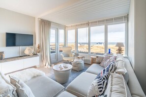 Ein modernes Wohnzimmer mit großem Fenster, Flachbildfernseher, bequemer Couch und gemütlicher Sitzecke.