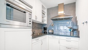 A modern kitchen with white cabinets, a stainless steel microwave, a built-in oven, a coffee maker, and a toaster. - 4 Person Apartment With sea View (De Koog)