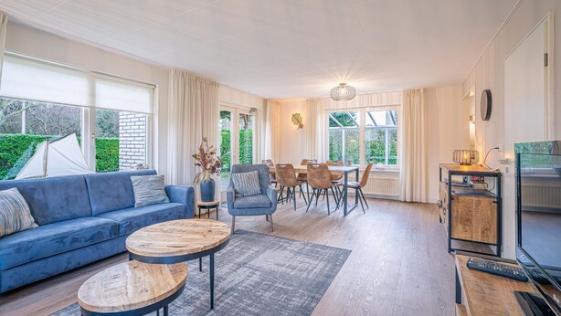 Ein geräumiges Wohnzimmer mit blauem Sofa, Holztisch und einem Essbereich mit Tisch und Stühlen.