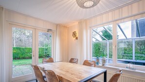 Ein Essbereich mit Holztisch und Ledersesseln, großen Fenstern mit Blick ins Grüne und einem dekorativen Wandbild.