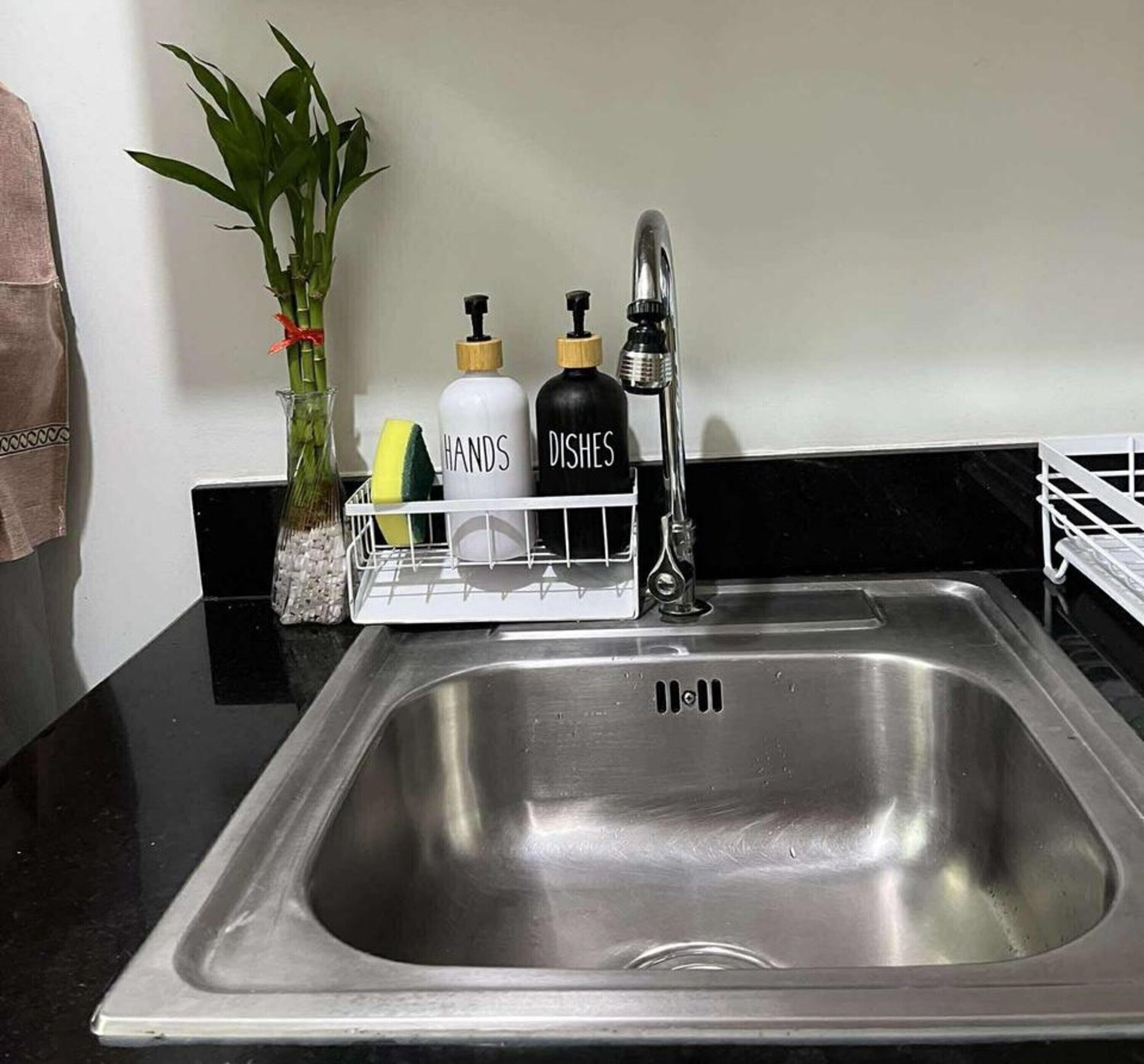 A stainless steel kitchen sink with a soap dispenser holder containing hand soap and dish soap.