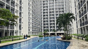 A modern building with a central swimming pool surrounded by greenery and palm trees. - Cozy Haven (Pasay)