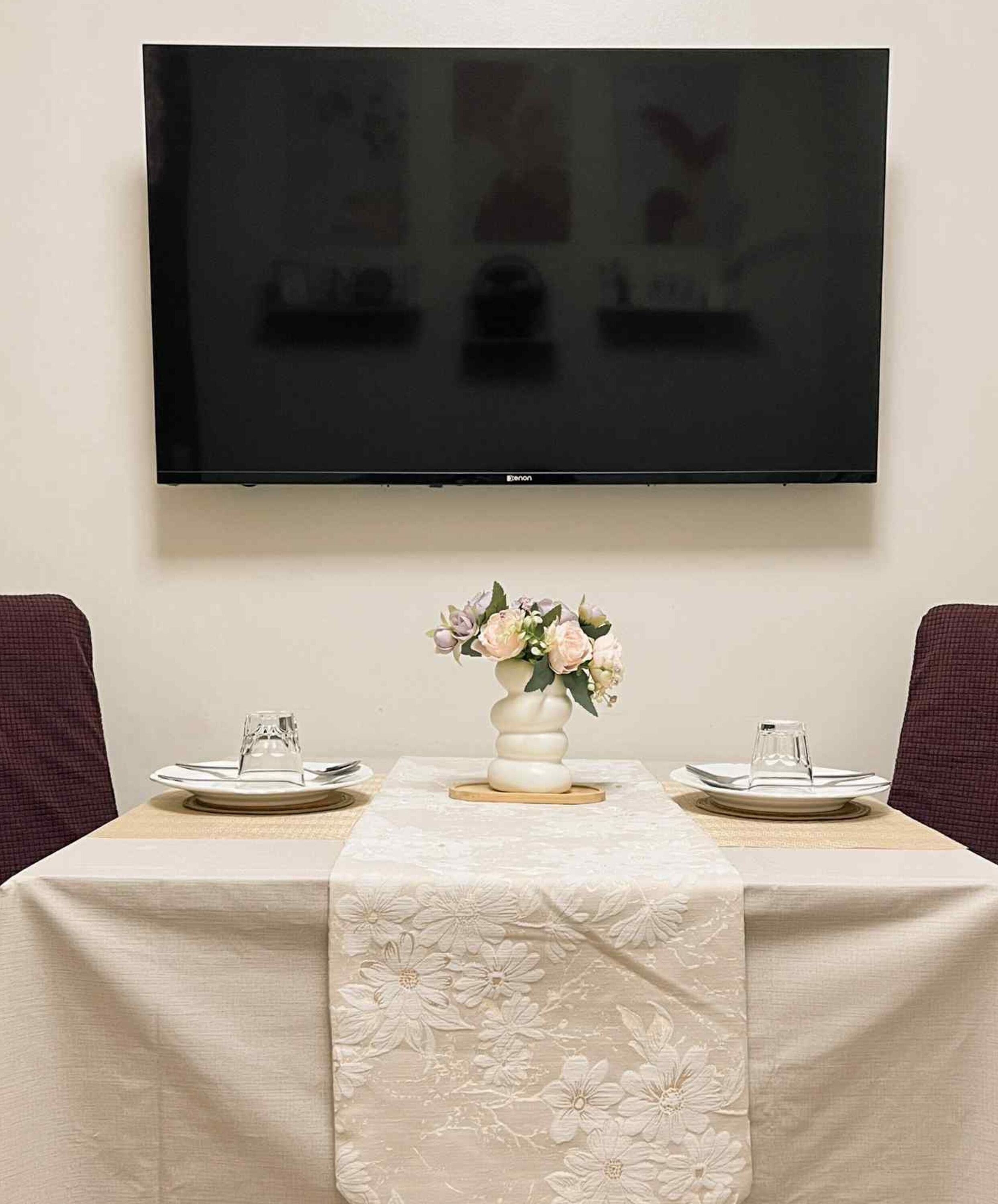 Un tavolo da pranzo con un runner floreale, un vaso con fiori e un televisore a schermo piatto montato a parete.