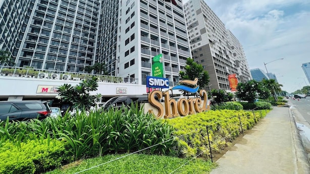 A modern hotel with a prominent 'Shore' sign, surrounded by lush greenery and tall buildings. - Cozy Haven (Pasay)