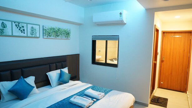 Een hotelkamer met een bed, kussens, een raam, een airconditioning en een deur.