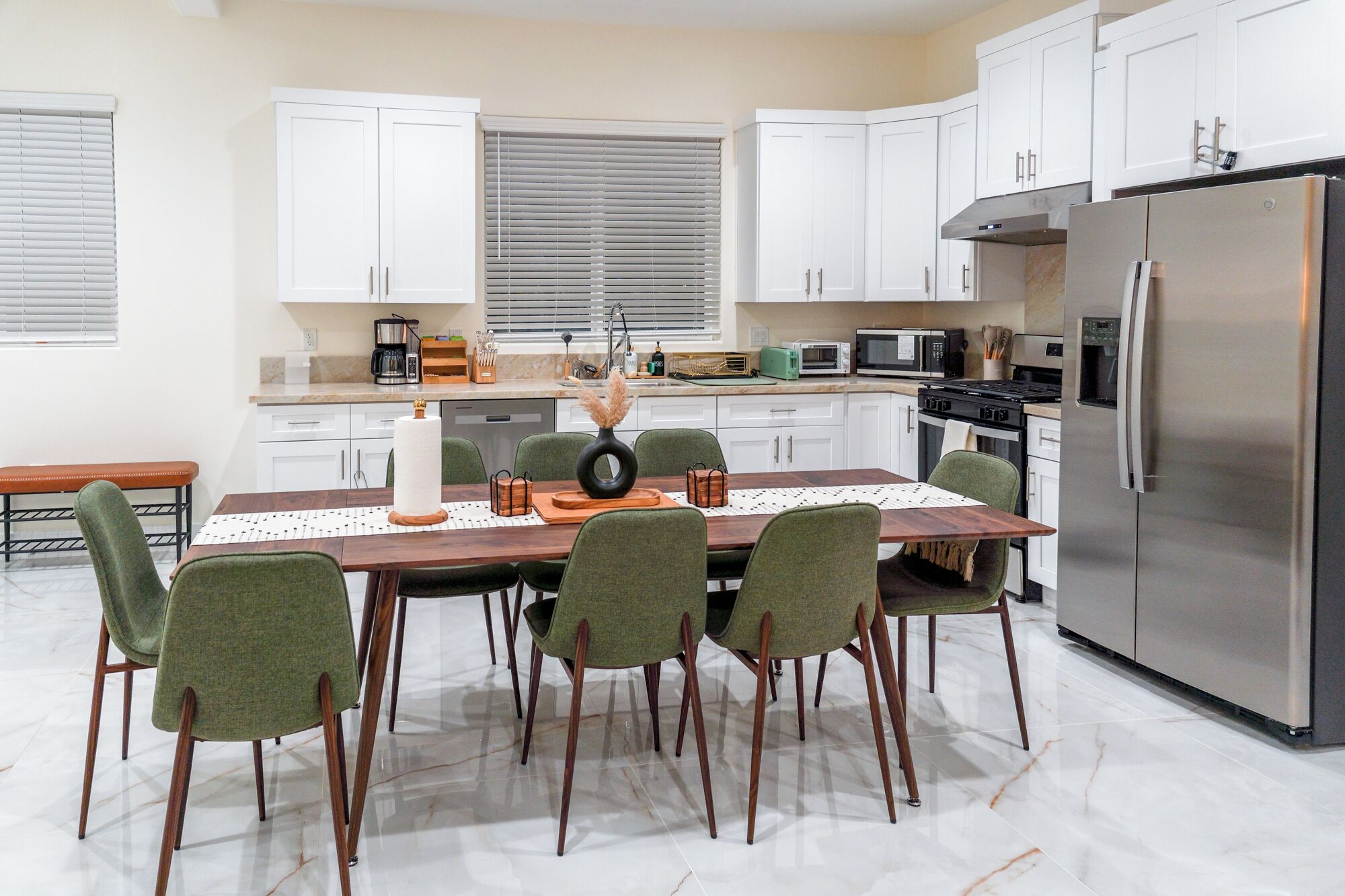 Een moderne keuken met witte kasten, een roestvrijstalen koelkast en een eethoek met een houten tafel en groene stoelen.