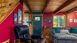 A cozy cabin interior with a wooden ceiling, a red wall, a blue door, a grey sofa, and a black leather chair. - Fir Tree Cabin | Grill, Fireplace (Packwood)